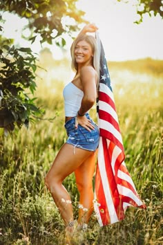 a beautiful woman holding an american flag posing for a photo in a field with tall grass