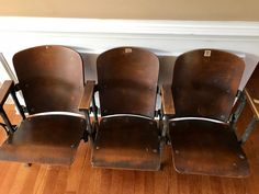 four brown school chairs lined up against a wall in a room with hard wood flooring