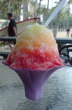 a pink and yellow ice cream sundae sitting on top of a table next to a surfboard