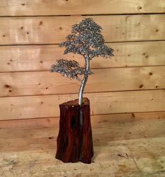 a metal tree sculpture sitting on top of a wooden stump in front of a wood wall