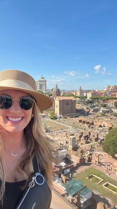 a woman wearing sunglasses and a hat standing on top of a building in the city