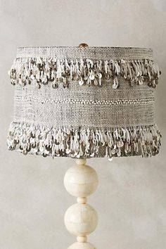 a white lamp that is sitting on top of a wooden base and has fringed trim around it