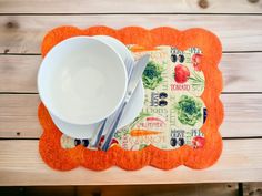 an orange placemat with a bowl, spoon and fork sitting on top of it