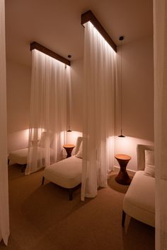 a room with three beds and two lamps on either side of the bed are white drapes hanging from the ceiling