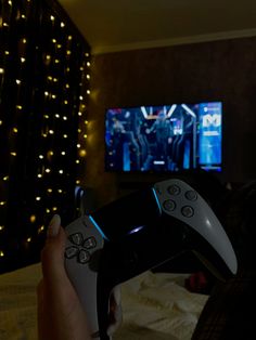 a person holding a video game controller in front of a tv with christmas lights on the wall