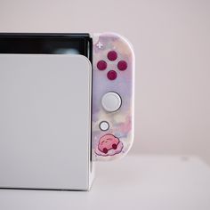 a nintendo wii game controller sitting next to a white box with pink buttons on it