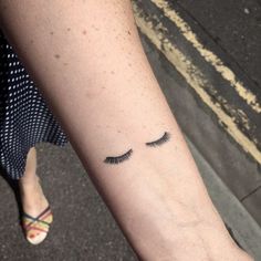 a woman's arm with a small tattoo on it that has eyelashes drawn out