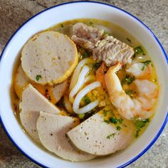 a white bowl filled with soup and meats on top of a stone countertop