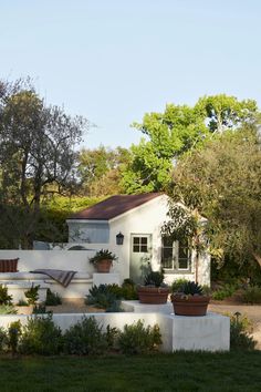 a white house with potted plants in front of it and trees around the building