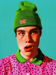 a young man wearing a green beanie and pink shirt with polka dots on it