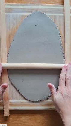 two hands are working on a piece of wood with a large oval shaped object in the background