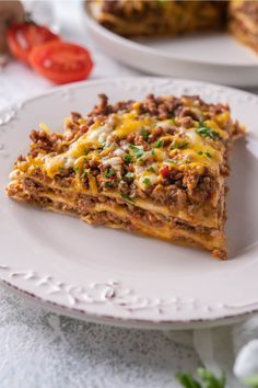 a slice of lasagna on a white plate with tomatoes in the back ground