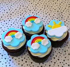 four cupcakes with blue frosting and rainbow designs on them sitting on a table