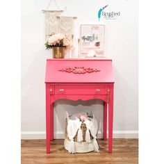 a pink table with flowers and pictures on the wall next to it in a room