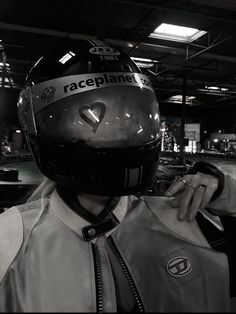 a man wearing a racing helmet and jacket in a garage with his hand on his shoulder