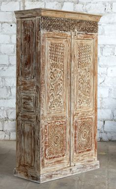 an old wooden cabinet with intricate carvings on the doors and bottom panel is standing against a white brick wall