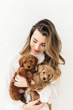 a woman is holding two poodles in her arms