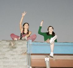 two young women sitting on top of a roof with their arms up in the air