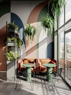 a living room filled with lots of furniture next to tall windows covered in potted plants