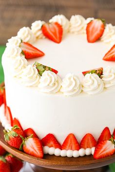 a white cake topped with strawberries on top of a wooden table next to green cloth