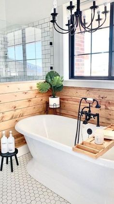 a white bath tub sitting under a window next to a wooden paneled bathroom wall