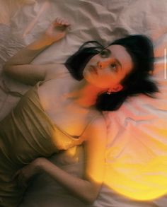 a woman laying on top of a bed next to a yellow light in the air