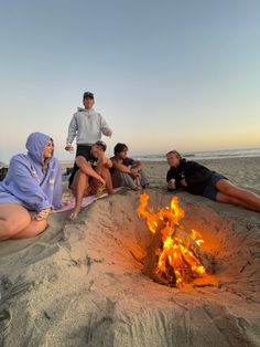 several people sitting around a campfire on the beach