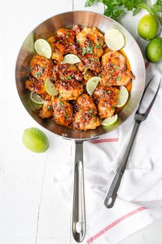 a pan filled with chicken and limes on top of a white table next to utensils