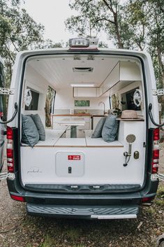 the back end of a white van with its doors open and pillows on it's bed