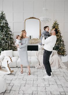 a man, woman and baby standing in front of a christmas tree