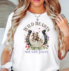 Feel the free-spirited energy of the wild west with this cowgirl riding a horse in a field of wildflowers t-shirt, featuring the inspiring phrase 'wild hearts, wild flowers'. A perfect addition to any nature lover's wardrobe, this tee embodies the carefree and adventurous spirit of the outdoors. Ideal for those who enjoy western style, horseback riding, and nature enthusiasts. Perfect for western-themed parties, outdoor events, and casual everyday wear. Product features - Available in multiple s Western Theme Party, Western Tee, Far West, La Girl, Cow Girl, Tees For Women, Wild Hearts, Casual Everyday, Horse Lover