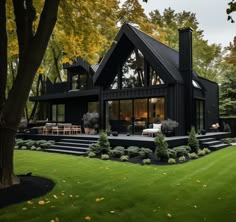 a large black house sitting in the middle of a lush green field next to trees