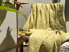 a yellow blanket sitting on top of a chair next to a potted plant