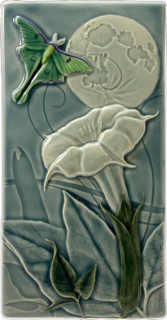 a ceramic tile with flowers and a butterfly on it's back side, in front of a full moon