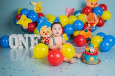 a baby is sitting in front of balloons and cake