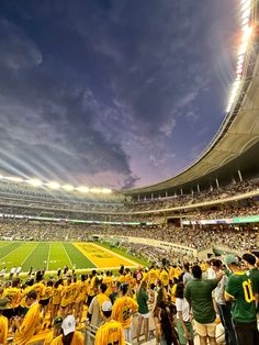 a stadium filled with lots of people standing on top of a field under a cloudy sky