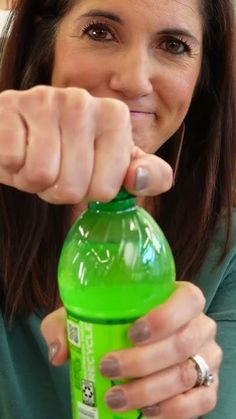 a woman holding onto a green bottle and pointing at the camera with her thumb on it