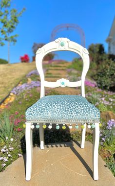 a white chair sitting on top of a cement slab in front of purple and green flowers