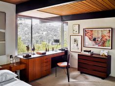 a bedroom with a desk, chair and large window overlooking the trees in the distance