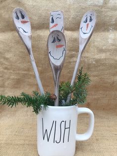 four spoons with faces painted on them are in a coffee cup that says wish