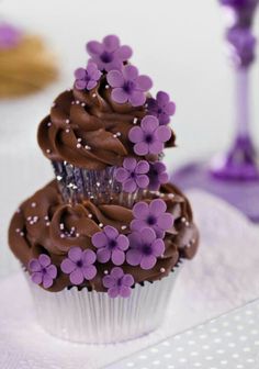 two cupcakes with chocolate frosting and purple flowers