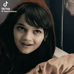 a young woman wearing a hoodie and looking at the camera while laying in bed