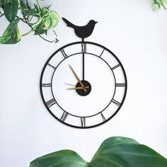 a clock with a bird sitting on it's face next to a green plant