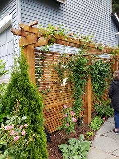 a woman standing in front of a wooden trellis with flowers growing on the side