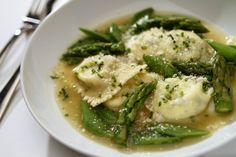 a white bowl filled with ravioli and asparagus