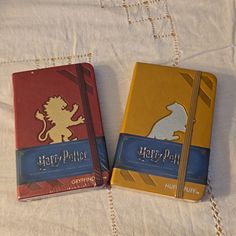 two harry potter notebooks sitting on top of a white bed sheet next to each other