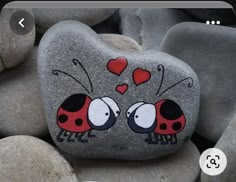 two ladybugs painted on a rock surrounded by some rocks with hearts drawn on them