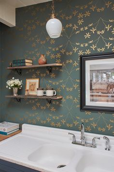 a kitchen sink under a hanging light in front of a wall with flowers on it