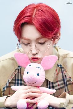 a woman with red hair and glasses holding a pink pig toy in front of her face