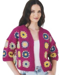 a woman is wearing a pink crocheted cardigan with flowers on the front